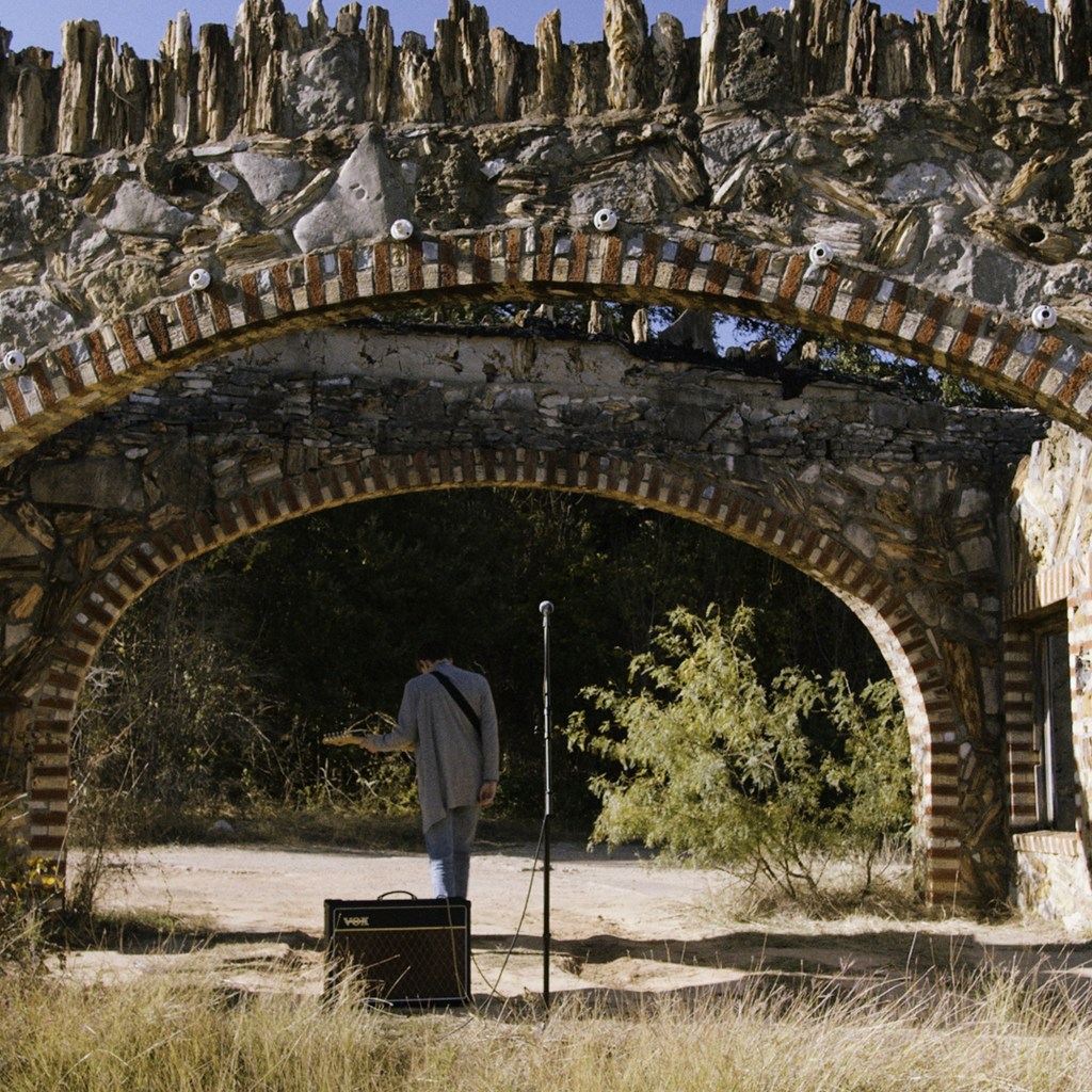 Artist playing a guitar under a stone brisdge.